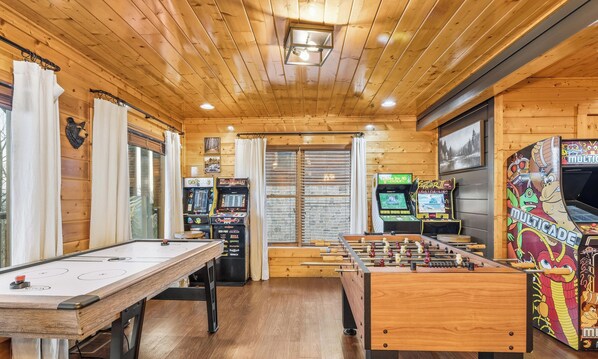 Ein Zimmer mit Holzboden, einer Tischfußballplatte, zwei Spielautomaten und einem Billardtisch.