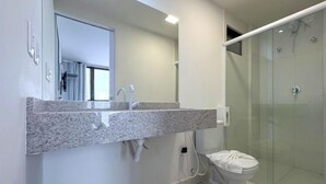 Et moderne badeværelse med en granitbordplade, en hvid vask, et spejl og en brusekabine i glas.
