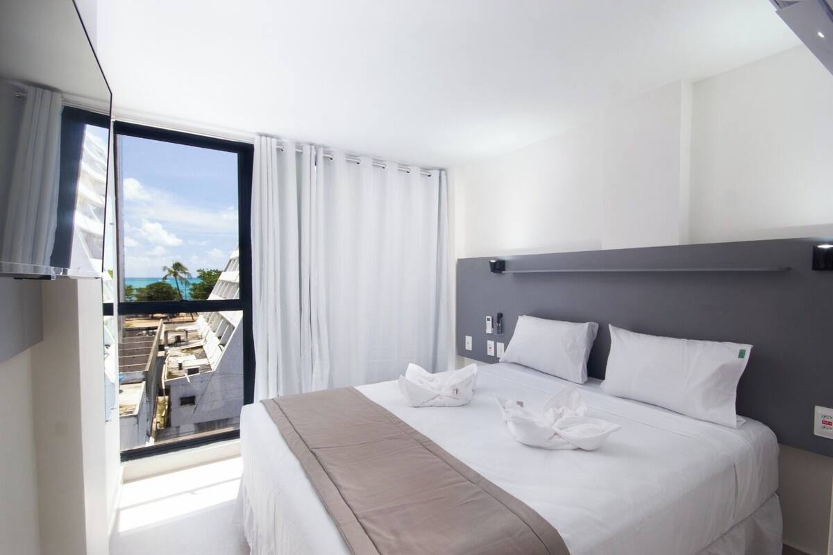 A hotel room with a large bed, a view of the cityscape, and a balcony with a view of the ocean.
