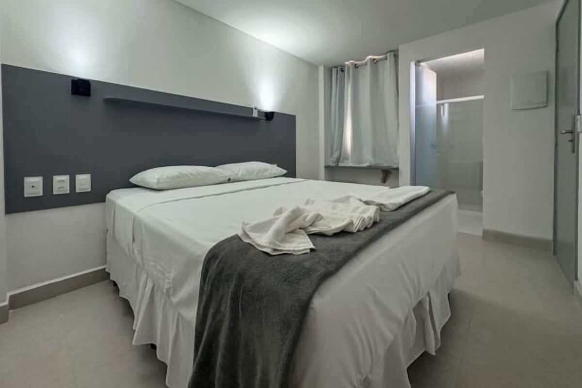 A modern bedroom with a large bed, a headboard, and a shower area.