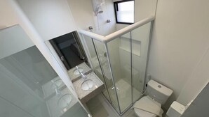 Et moderne badeværelse med bruseniche i glas, toilet og håndvask.