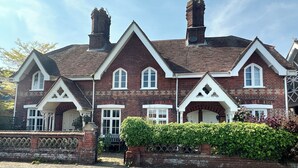 A large, two-story brick house with multiple chimneys, white-framed windows, and a gated entrance. - Orford Holiday Cottage (Orford)