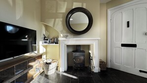 A modern living room with a fireplace, a television, and a large mirror. - Orford Holiday Cottage (Orford)