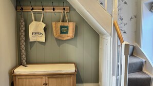 A wooden bench with a cushion, a coat rack with two bags, and a staircase with patterned wallpaper. - Orford Holiday Cottage (Orford)