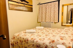 Un dormitorio con colcha estampada, un radiador, una ventana con cortinas y un espejo con marco decorativo.