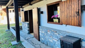 Un espacio exterior techado con escalones de piedra, puertas de madera y una ventana con un macetero.