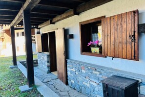Ein überdachter Außenbereich mit Steinstufen, Holztüren und einem Fenster mit Blumenkasten.