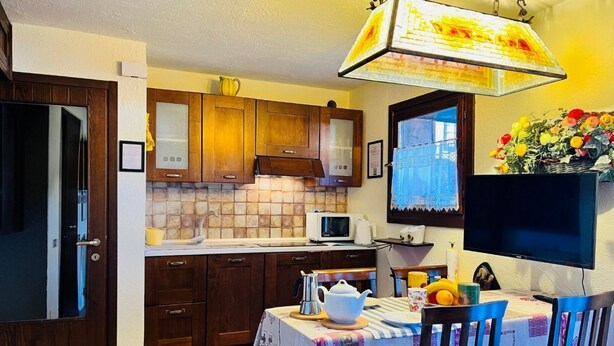 Una cocina con armarios de madera, microondas, una mesa con mantel y un televisor.