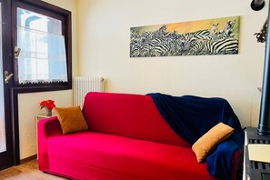 Ein rotes Sofa mit zwei Kissen, ein Heizkörper, ein Fenster mit Spitzenvorhängen und ein Zebra-Gemälde an der Wand.
