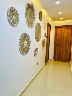 A hallway with a wooden door, white walls, and various woven wall hangings. - Modern Scandinavian Inspired 1-Bed|Mini Golf Area (Ikeja)