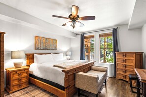 A bedroom with a large bed, a ceiling fan, a window with curtains, a painting on the wall, and wooden furniture. - Main Street - Just Steps Away | Private Hot Tub |Managed by Park City Lodging (Park City)
