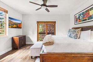 A bedroom with a bed, a nightstand, a wooden dresser, a ceiling fan, a window with a view, and a painting on the wall. - Main Street - Just Steps Away | Private Hot Tub |Managed by Park City Lodging (Park City)