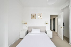 A minimalist hotel room with a large bed, white walls, and two framed pictures. - Argyl | Stanhope Gardens: Bright 2 bedroom Apt. (London)