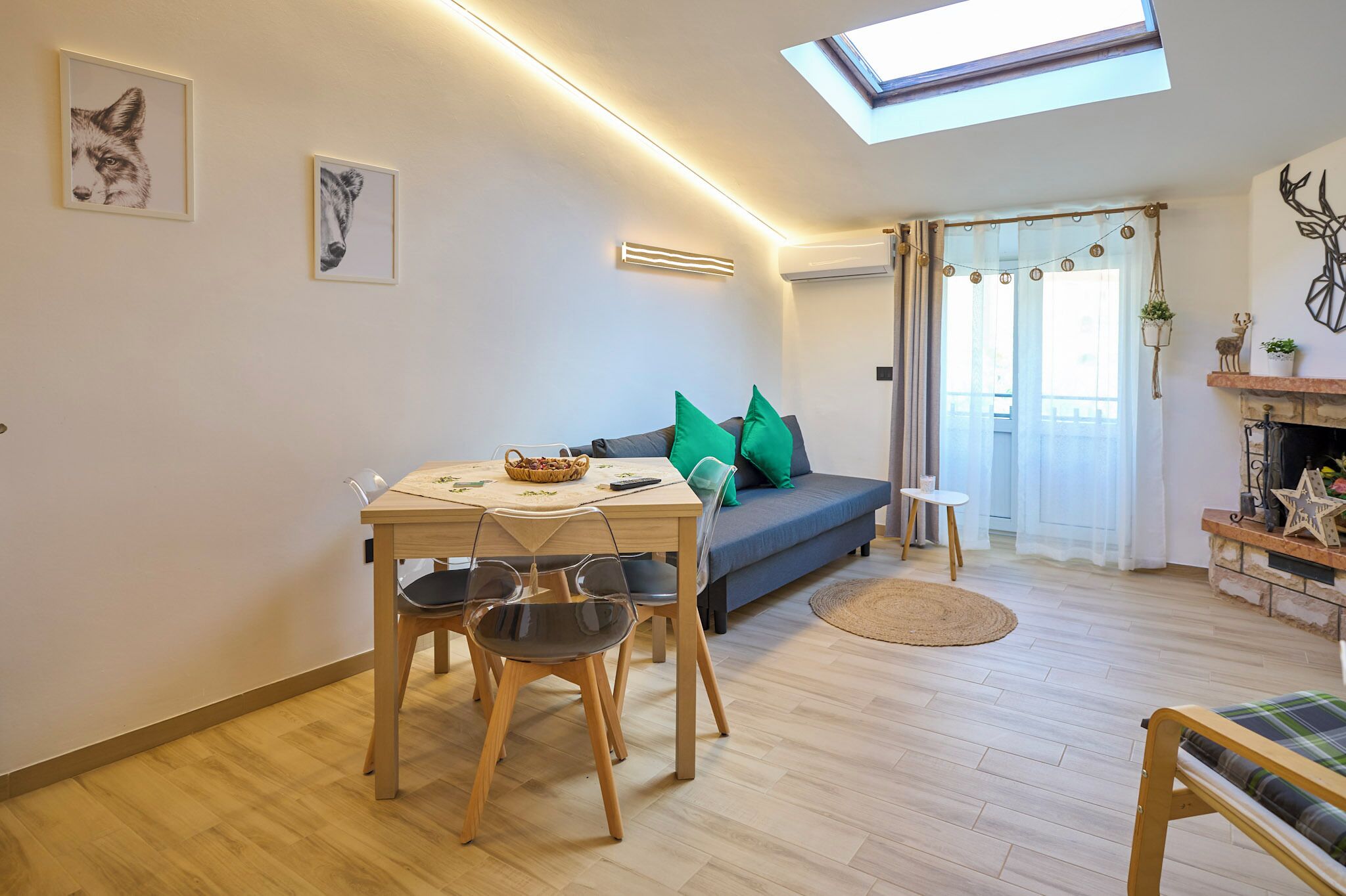Un espacio moderno de estar con comedor, sofá con cojines verdes, una mesita y una chimenea.