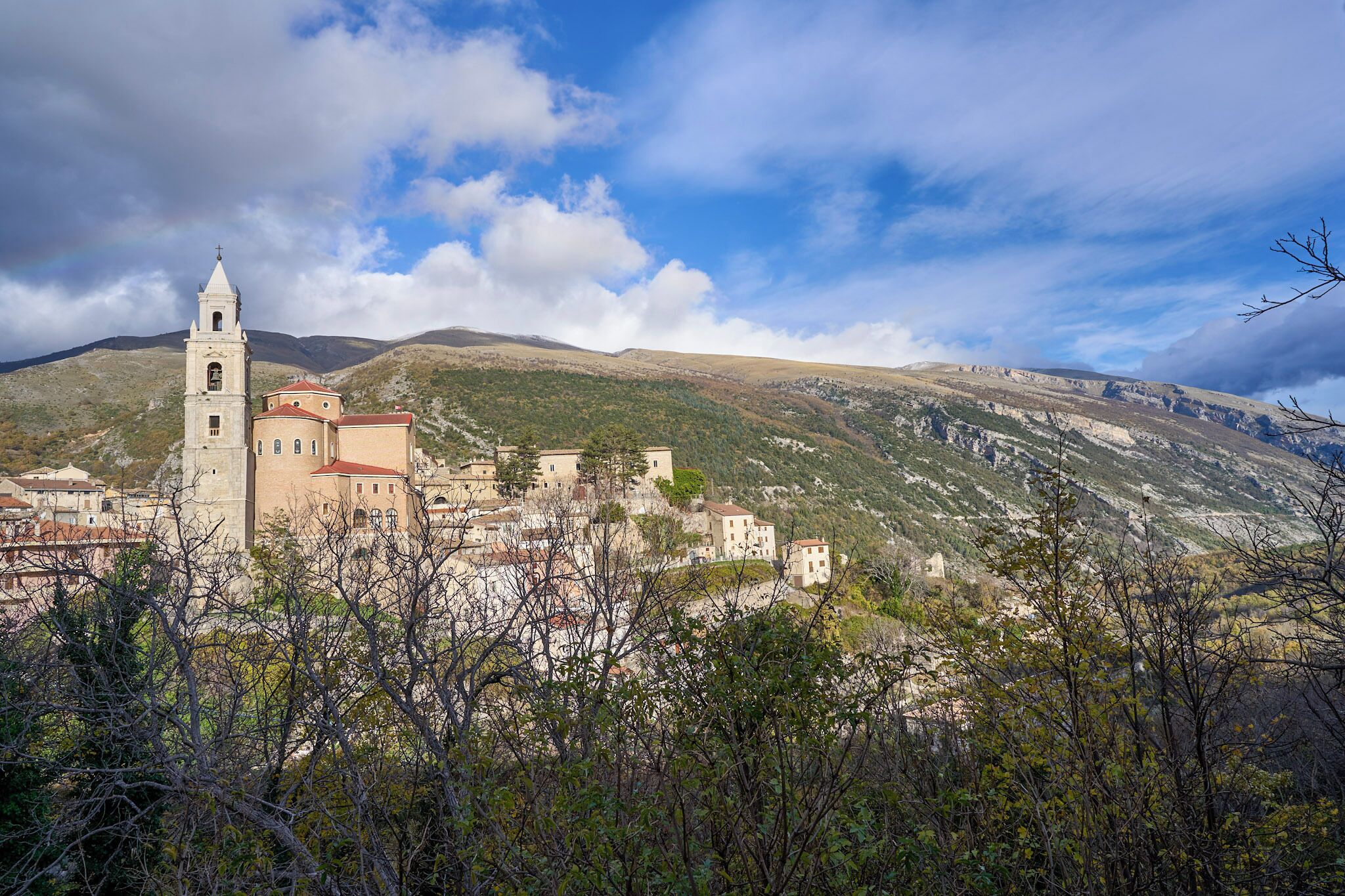 A mountainous landscape with a church featuring a bell tower and a red-roofed building.