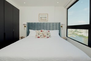 Un dormitorio con una cama grande, vistas a un paisaje urbano y un cuadro en la pared.
