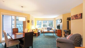 A cozy living room with a dining area, a fireplace, and large windows. - The Haven at Blueberry Hill - Mount Washington ski-in/out (Comox-Strathcona C)