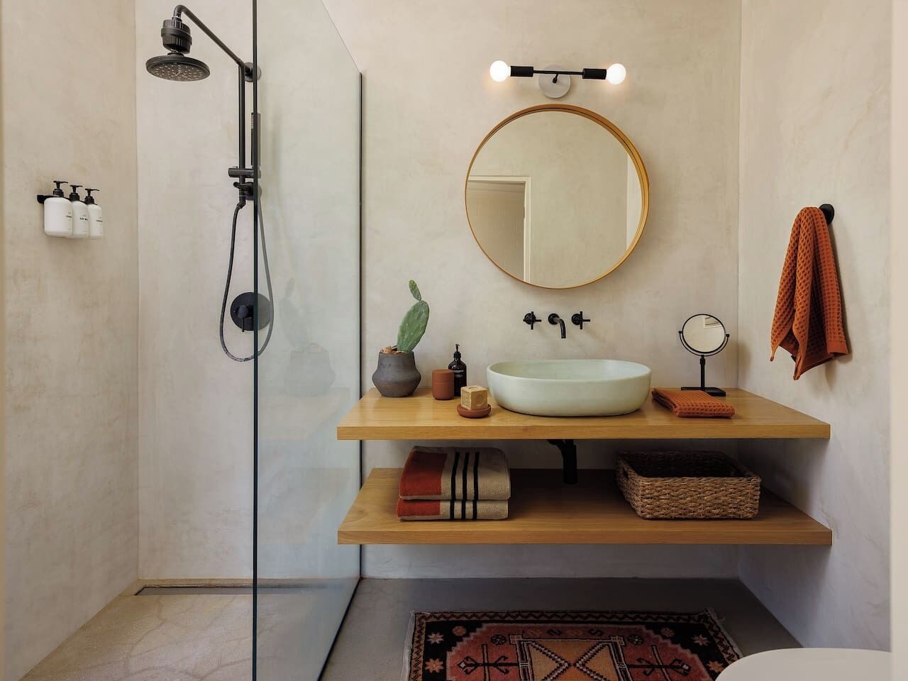 A modern bathroom with a freestanding shower, a round mirror, a sink, and a towel rack.