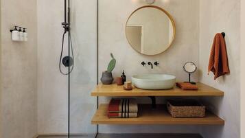 A modern bathroom with a freestanding shower, a round mirror, a sink, and a towel rack.