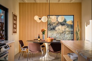Un'area pranzo moderna con un tavolo rotondo, due sedie, un vaso con fiori e una grande finestra vista deserto.