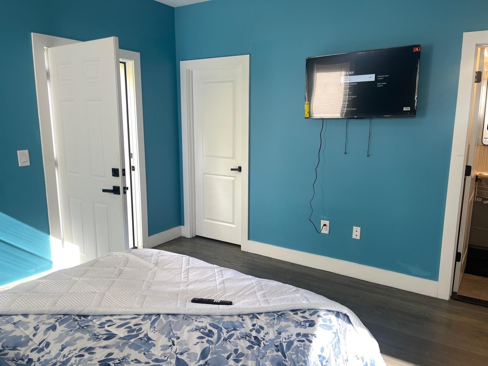 Un dormitorio con una cama, dos puertas blancas, un televisor montado en la pared y un enchufe.