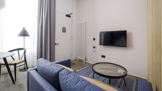 A modern living room with a sofa, a small table, a TV mounted on the wall, and a window with curtains. - Argyl | Abbey Gate: Studio 11 (Edinburgh)