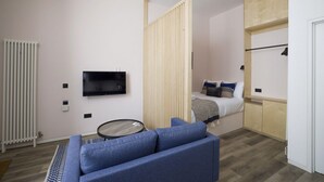 A modern room with a sofa, a TV, a bed, a radiator, and a wooden partition. - Argyl | Abbey Gate: Studio 11 (Edinburgh)