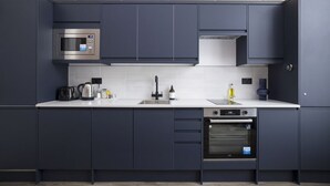 A modern kitchen with dark cabinets, a microwave, a kettle, a sink, and an oven. - Argyl | Abbey Gate: Studio 11 (Edinburgh)