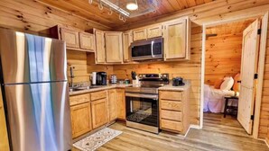 A compact kitchen with wooden cabinets, a refrigerator, a microwave, and an oven. - Secluded 2 Bedroom Timber Ridge Cabin- Hot Tub, Lake Boat Ramp 1 Mile, Fishing (Louisa)