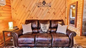 A wooden cabin interior with a leather sofa, a 'WELCOME' sign, and a lamp. - Secluded 2 Bedroom Timber Ridge Cabin- Hot Tub, Lake Boat Ramp 1 Mile, Fishing (Louisa)