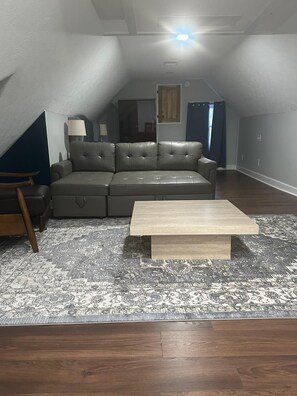 Uma sala de estar com sofá seccional, mesa de centro de madeira e tapete estampado.