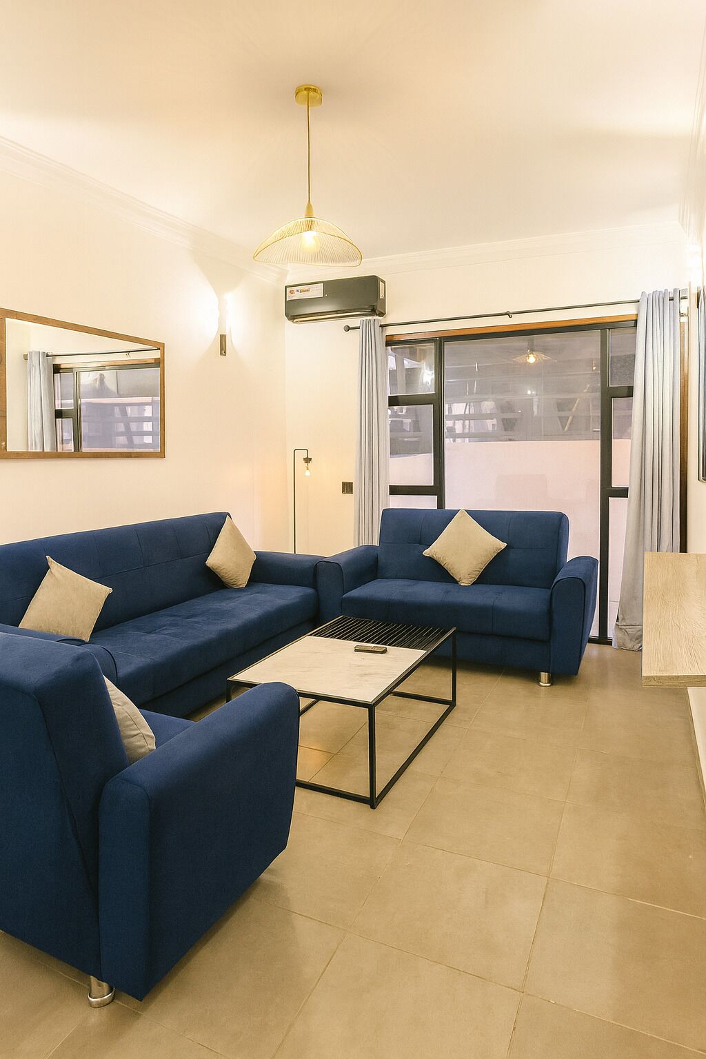 Een moderne woonkamer met twee blauwe banken, een salontafel en een groot raam met gordijnen.