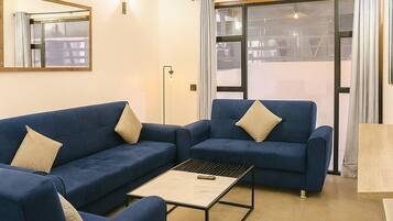 Un moderno salón con dos sofás azules, una mesita de centro y un amplio ventanal con cortinas.