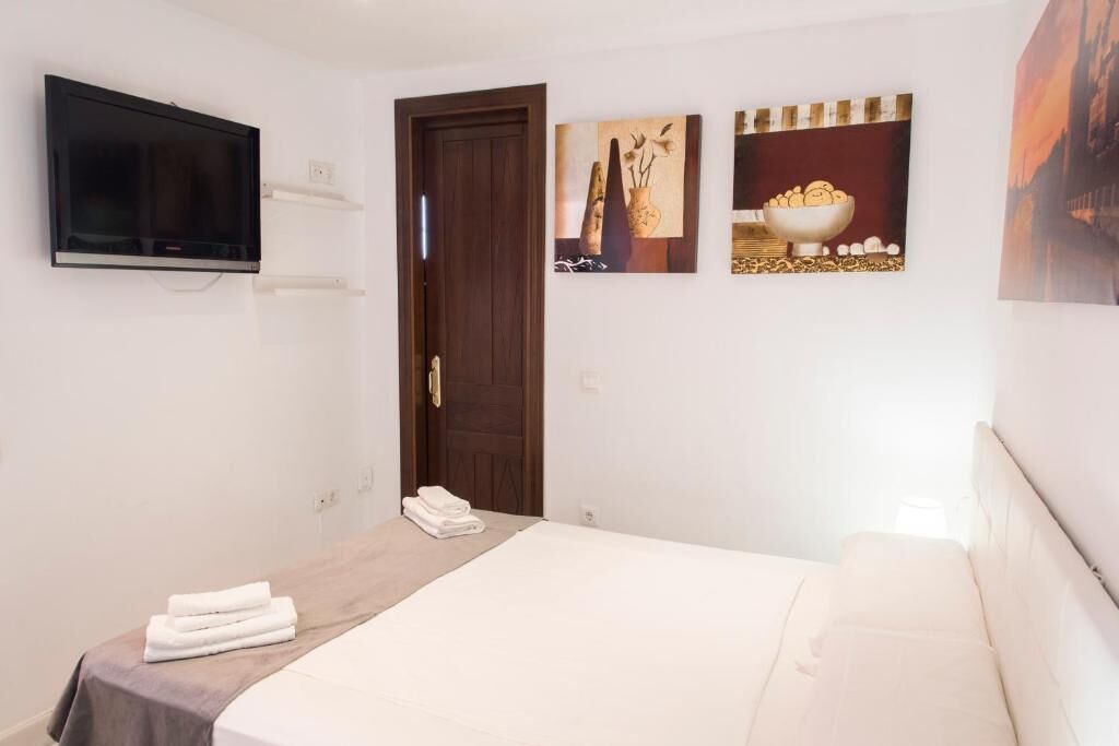Una habitación de hotel con cama, televisor montado en la pared y obras de arte en las paredes.