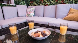 A glass table with a bowl of pastries and two glasses of orange juice in front of a grey sofa with floral cushions. - Night In Sevilla (Seville)