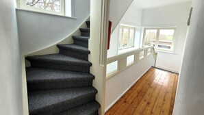 A staircase with a wooden finish, white walls, and a view of the outdoors through windows. - Vakantiehuis d'Ereplatse (Zuienkerke)