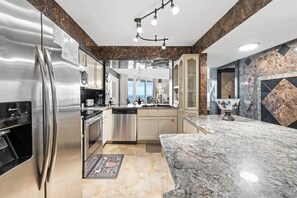 A modern kitchen with stainless steel appliances, a marble countertop, and a view to the outside. - 3BR Beachfront Dunes of Panama 3 Pools Sleeps 10 (Panama City Beach)