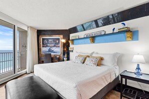 A hotel room with a large bed, a view of the sea, a balcony, and a 'Beach House' sign on the wall. - 3BR Beachfront Dunes of Panama 3 Pools Sleeps 10 (Panama City Beach)