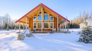 Eine Blockhütte mit rotem Dach, großen Fenstern und einer Veranda mit Stühlen.
