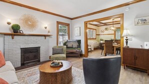 Ein Wohnzimmer mit Kamin, ein Essbereich und eine durch einen offenen Durchgang sichtbare Küche.