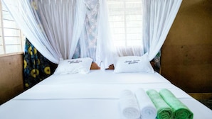 Un lit avec du linge de lit blanc, deux oreillers et des serviettes roulées, aux couleurs blanc et vert.