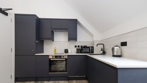 Uma cozinha moderna com armários escuros, micro-ondas, chaleira e forno embutido.