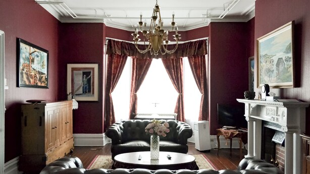 Ein Wohnzimmer mit einer schwarzen Ledersofa, einem runden Couchtisch mit einer Vase, einer Chandelier, einem Kamin und einem großen Fenster mit Vorhängen.