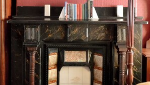 Ein Kamin mit einem darüberhängenden gerahmten Gemälde, flankiert von Büchern und einem Kerzenständer.