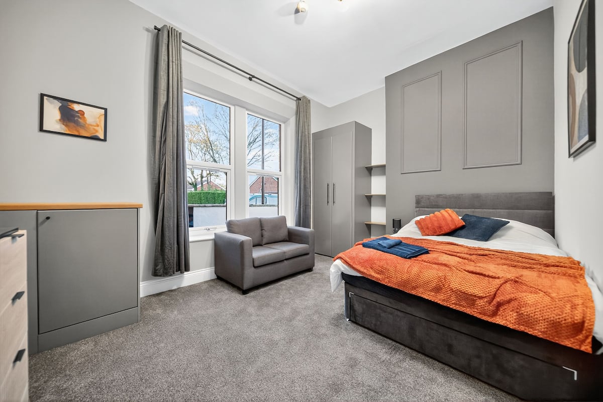 A bedroom with a bed, grey wardrobe, grey sofa, and a window with curtains.