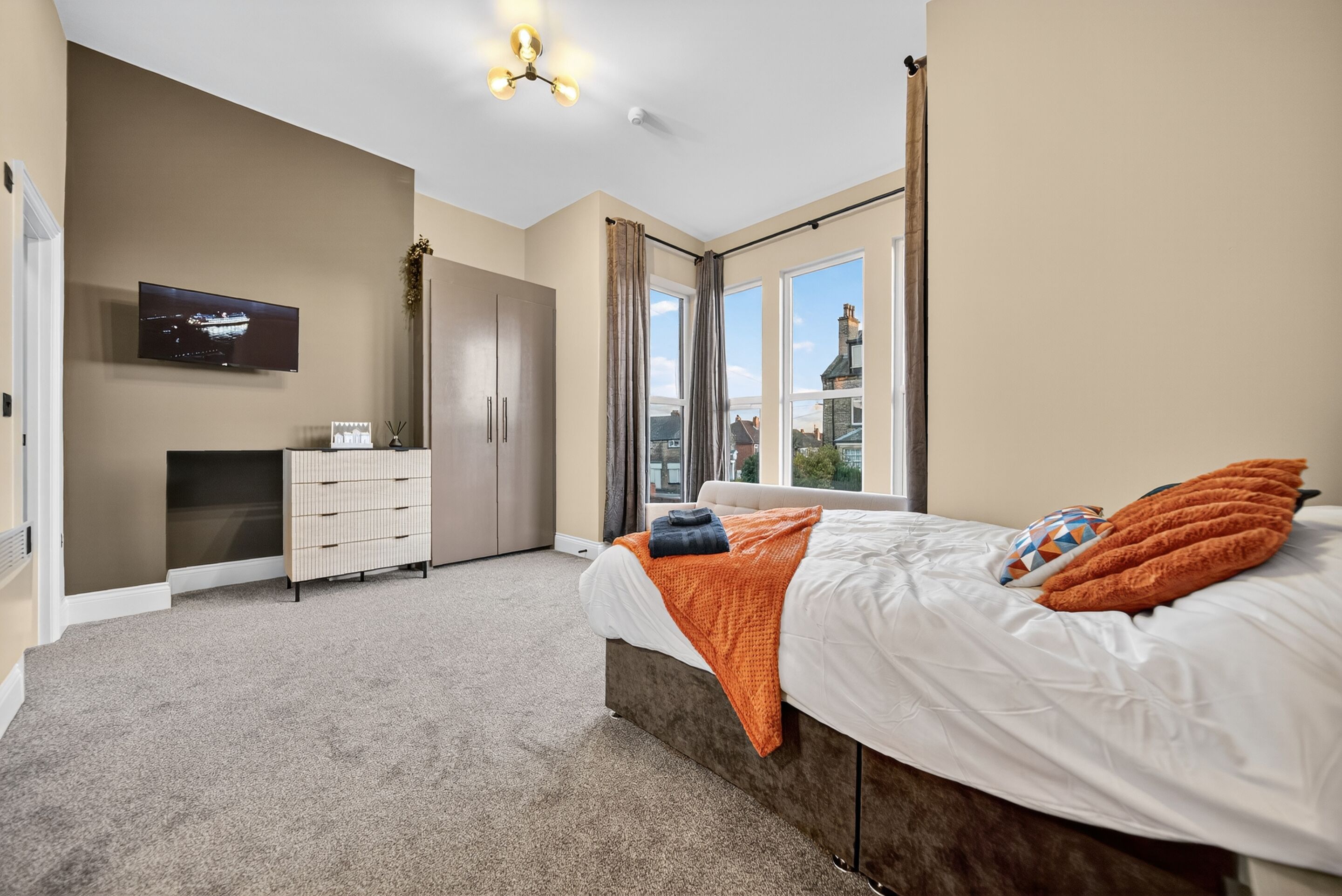 A bedroom with a bed, a TV, a wardrobe, and a window with a view.