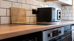 A kitchen with white tiled backsplash, a wooden cutting board, a black microwave, and a stainless steel oven. - Rosemont Road (Leeds)