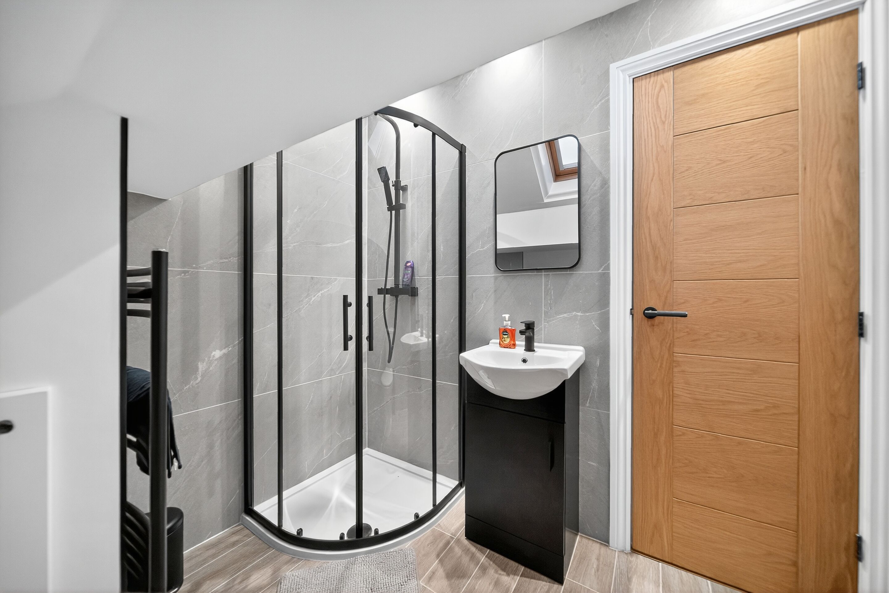 Ein modernes Badezimmer mit einer gläsernen Duschkabine, einer Holztür und einem weißen Waschbecken.