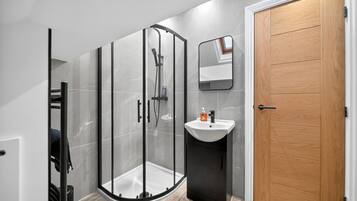 Ein modernes Badezimmer mit einer gläsernen Duschkabine, einer Holztür und einem weißen Waschbecken.