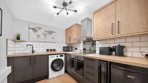 A modern kitchen with dark cabinets, a washing machine, an oven, and a dishwasher. - Rosemont Road (Leeds)